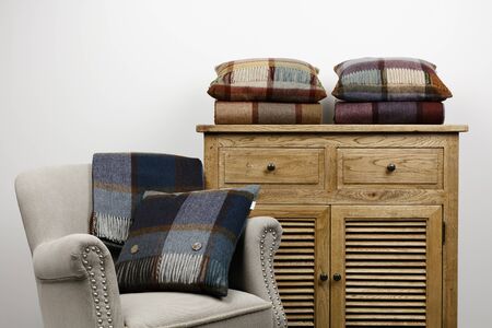 Chair and side cabinet with blue and maroon checked cushions and throws, against  a white background.の写真素材