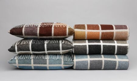 Two piles of colourful cushions and throws, on a light grey background.の写真素材