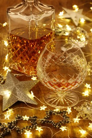 Crystal glass of brandy and a crystal brandy decanter with christmas lights and silver stars, on a wooden tableの写真素材