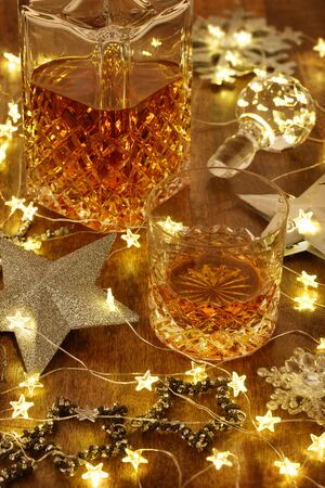 Crystal glass of whisky and a crystal whisky decanter with christmas lights and silver stars, on a wooden tableの写真素材