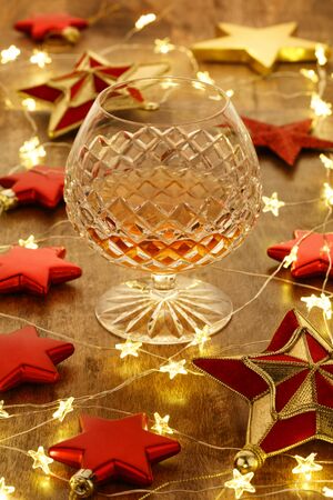 Crystal brandy glass with with christmas lights and red stars decorations, on a wooden tableの写真素材