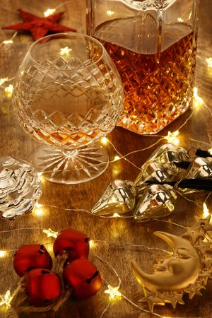 Crystal glass of brandy and a crystal brandy decanter with christmas lights and christmas bell decorations, on a wooden tableの写真素材
