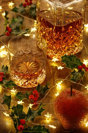 Crystal whisky decanter  and a glass of whisky with christmas lights and holly berries, on a wooden tableの写真素材