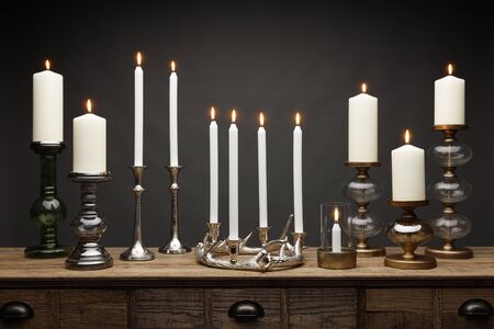 A group of candle sticks and candle holders and glowing candles, shot on a wooden table, with a dark grey backgroundの写真素材