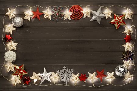 A border of golden star christmas lights and sparkling christmas decorations, on a distressed dark wooden board backgroundの写真素材