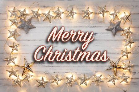 A border of golden star christmas lights, and star baubles, with Merry Christmas written in the middle, on a destressed woodern backgroundの写真素材