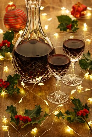 A decanter of port and crystal glasses with christmas lights, baubles, holly berryies and christmas decorations, on a wooden tableの写真素材