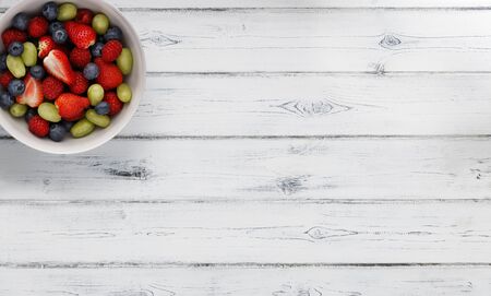 A bowl full of delicious fresh summer fruits, shot on a distressed white wooden background, with space for copyの写真素材