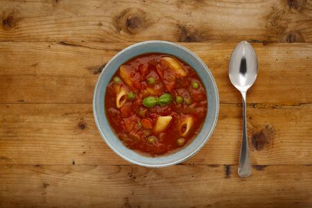 A bowl of delicious minestrone soup, topped with a sprig of basil, in a rustic bowl, on a wooden background, with a spoon.の写真素材