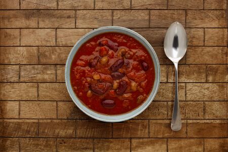 A bowl of delicious chilli bean soup, in a rustic bowl, on a checked wooden background, with a silver spoon.の写真素材