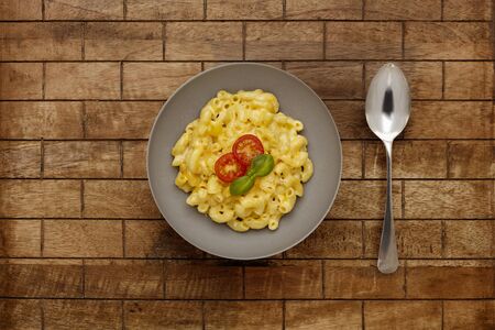 A bowl of delicious Macaroni and cheese, topped with cherry tomatoes and basil, on a checked wooden...