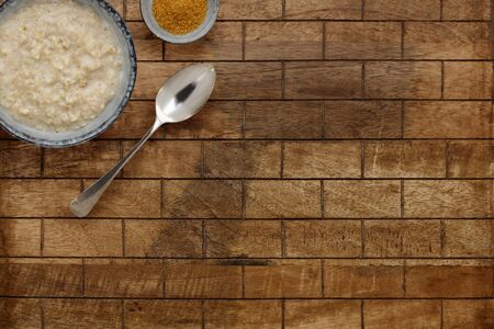 A nutritious bowl of porridge, a small bowl of brown sugar with a sppon, on a checked wooden background with copy spaceの写真素材