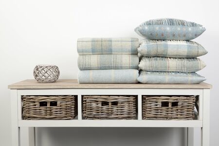 Sideboard style white wooden table with blue coloured cushions, throws and ornaments and wicker baskets on a white backgroundの写真素材