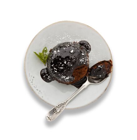 An individual chocolate sponge cake, with a sticky chocolate sauce, on a white plate with a spoon, isolated on white with a darop shadow.の写真素材