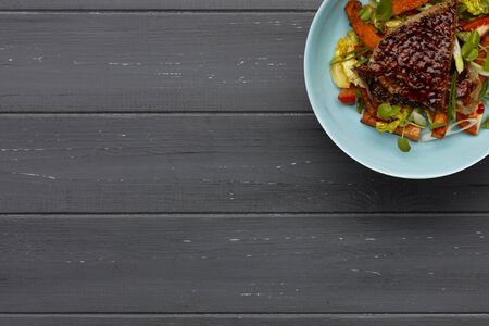 A delicious bowl of BBQ rump steak, sweet potatoe chips and vegetables, in a light blue bowl on a distressed dark wooden backgroundの写真素材