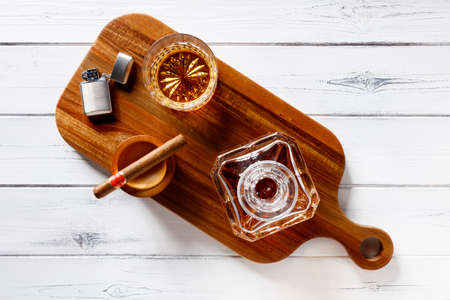 View of a crystal glass and decanter full of golden whisky, cigar and petrol lighter on a wooden...