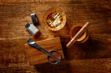 View of a crystal glass of golden whisky, cigar and cigar cutter and petrol lighter, shot from above...