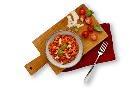 A bowl of delicious tomato pasta in a rustic bowl, garnished with a sprig of basil, placed on a wooden serving board with napkin, isolated on white with a drop shadowの写真素材