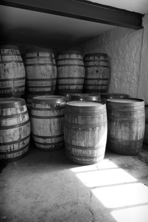 Black and white old whisky barrels, stacked in a warehouse ready to fill with raw spirit and leave to mature over time, in a dusty warehouse with light shinning through a windowの写真素材