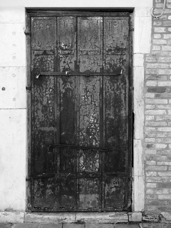 Old wooden door with peeling paint and rusting hinges in an ancient brick wallの写真素材