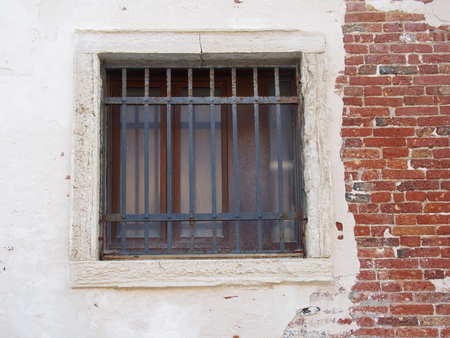 window with bars in an old distressed white and brick wall