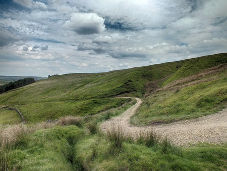 winding hillside pathway in rugged moorland with grass and clouds