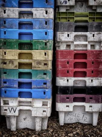 fish transportation boxes in different colors stacked on a beach in a harborの写真素材