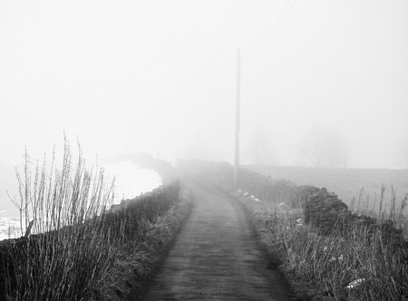 fog on a country lane vanishing into the distance with with snow and stone wallsの写真素材