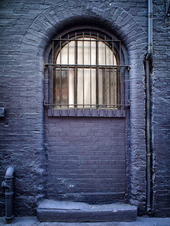window with bars in a blue painted brick wall with pipes and worn step partly blocked up
