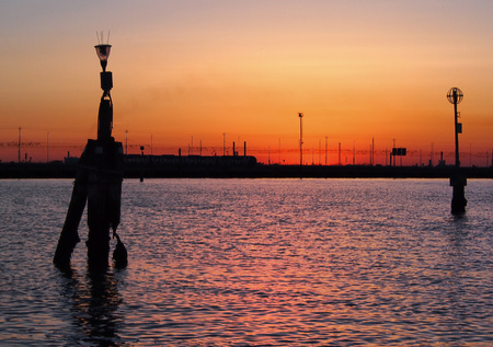 sunset on the lagoon in venice with orange sky reflected in the water and bridge in the backgroundの写真素材
