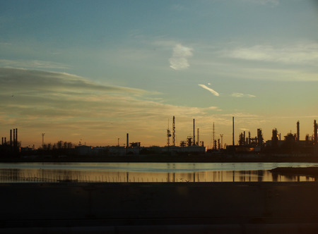industrial landscape on the coast with pipes towers and refinery chimneys from manufacturing with reflections of buildings in the sea at sunsetのeditorial素材