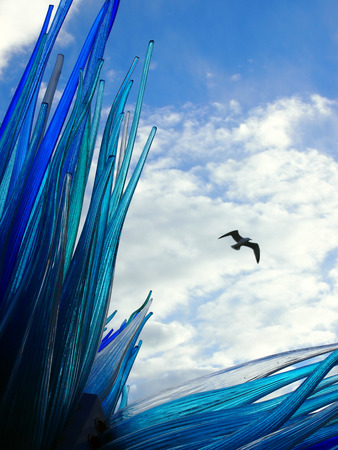 Blue glass sculpture in murano venice with bird flying in summer sky with white cloudsの写真素材
