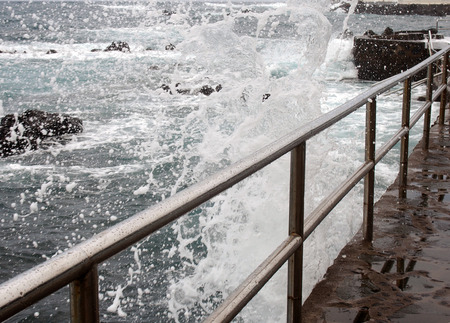 High dramatic waves breaking over a seafront promenade with white surf steel railings and blue seaの写真素材