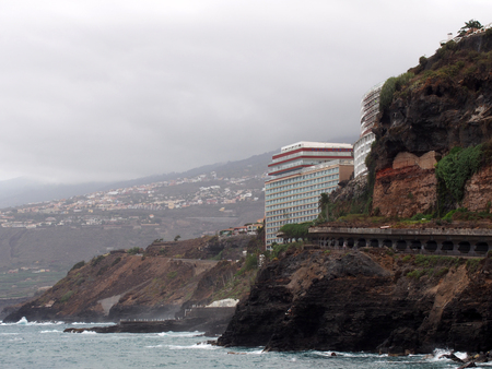 the cliffs and sea at puerto de la cruz in tenerife with waves the town and typical cloudsのeditorial素材