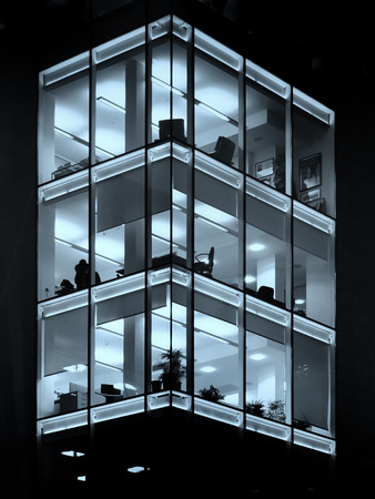 modern office building illuminated at night blue geometric windowsの写真素材