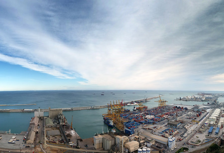 view of barcelona docks and harbour with shipping containers being loaded, warehouses grain silos and railway lines with surrounding city industrial area and open seaの写真素材