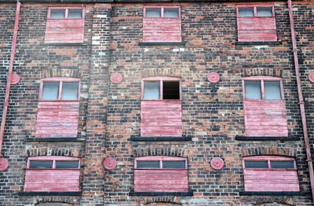 facade of a derelict abandoned old brick industrial building with red painted broken boarded up decaying windowsの写真素材