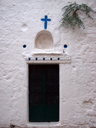 beautiful old rural church door in Kos Greece in a white painted wall with plant growing from it and blue cross and decorationの写真素材