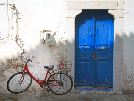 colourful summer scene of an old red bike outside a greek house with whitewashed walls and a blue painted door in bright sunlight in Kosの写真素材