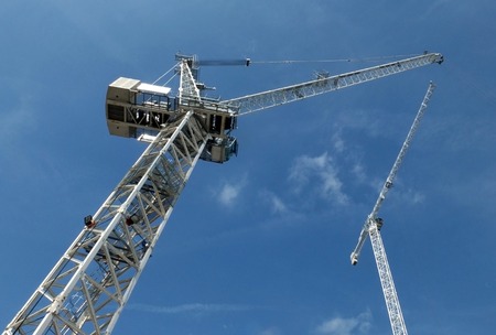 a perspective view of two tall white construction cranes on a building site against a blue sky with cloudsの写真素材