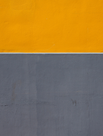 yellow and grey areas of paint on a rough textured concrete wall divided by a horizontal white stripeの写真素材