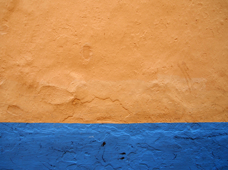An orange painted old textured distressd concrete wall with a bright blue stripe running along the bottom of the imageの写真素材