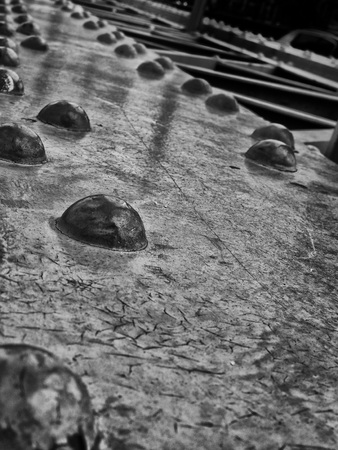 close up perspective view of old black steel girders on a bridge with large round rivets and cracked black shiny paintの写真素材