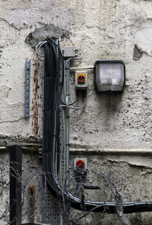 an external security light mounted on an old shabby external wall with messy wiring and barbed wireの写真素材