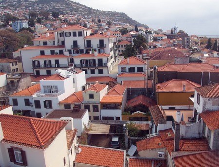 an aerial view of funchal in madeira showing red tiled roofs of old white buildings with the coast in the distanceの写真素材