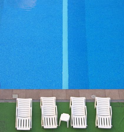 aerial view of white sunbeds at the side of a blue swimming pool with bright water and a stripe in the tilesの写真素材