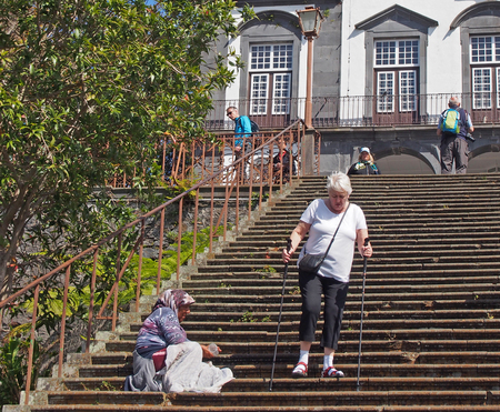 funchal, madeira, portugal - 14 march 2019: a tourist walking around an old lady begging on the steps of the historic Church of Our Lady of Monte in funchalのeditorial素材