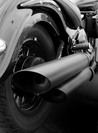 monochrome close up of the back of a vintage motorcycle with rear wheel mudguard and wide exhaust pipesの写真素材