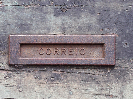 an old rusting iron letterbox in a black wooden door with chipped peeling paint with the word correio, translation from portuguese is mailの写真素材