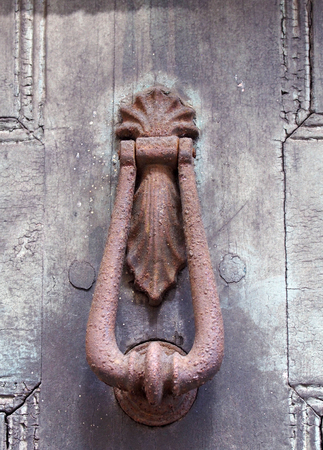 close up of an old brown rusty ornamental iron door knocker on a faded black painted house doorの写真素材